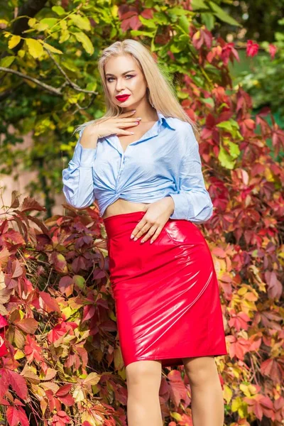 秋天的公园里 穿着蓝色衬衫 红色短裙和皮夹克的漂亮女人站在那里摆姿势 漂亮的女人 金发碧眼 — 图库照片