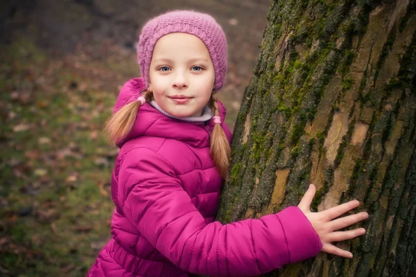 Klein meisje in de buurt van boom in de herfst of winter park. — Stockfoto