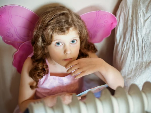 Little girl wearing butterfly wings get a warm near radiator — Stock Photo, Image