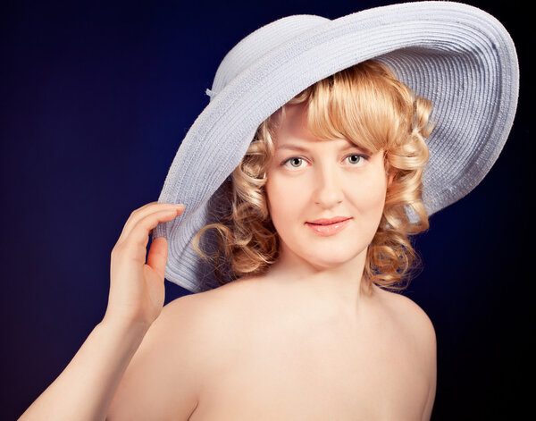 Portrait of a beautiful female model wearing big blue hat on dark background