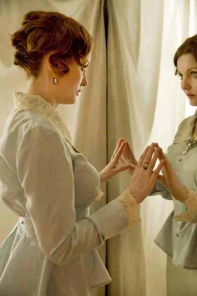 A young girl sitting in front of a big mirror and looking away o