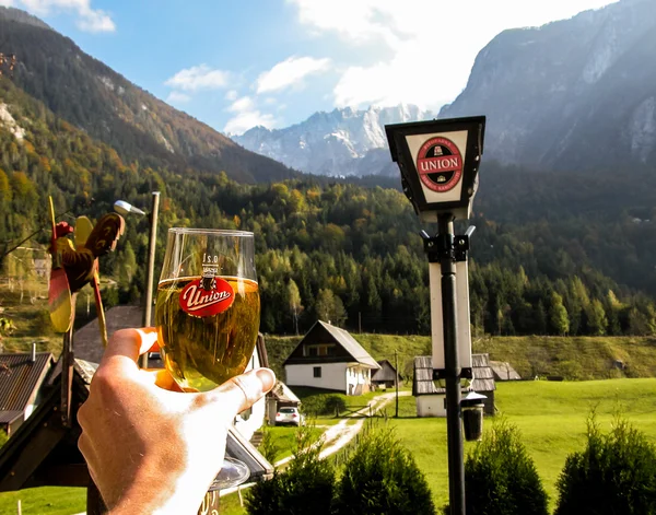 Mano masculina sosteniendo un vaso de cerveza Union contra el paisaje alpino — Foto de Stock