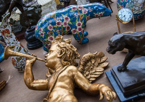 Anjo bebé dourado a tocar trompete. Estatueta de urso colorido no fundo. Mercado de pulgas em Paris . — Fotografia de Stock