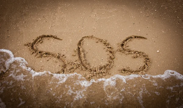 SOS inscription on beach sand washed by sea wave — Stock Photo, Image