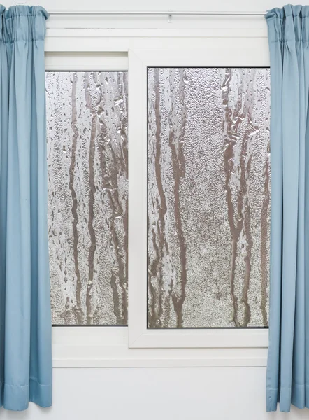 Белое окно с голубыми шторами в дождливый день — стоковое фото