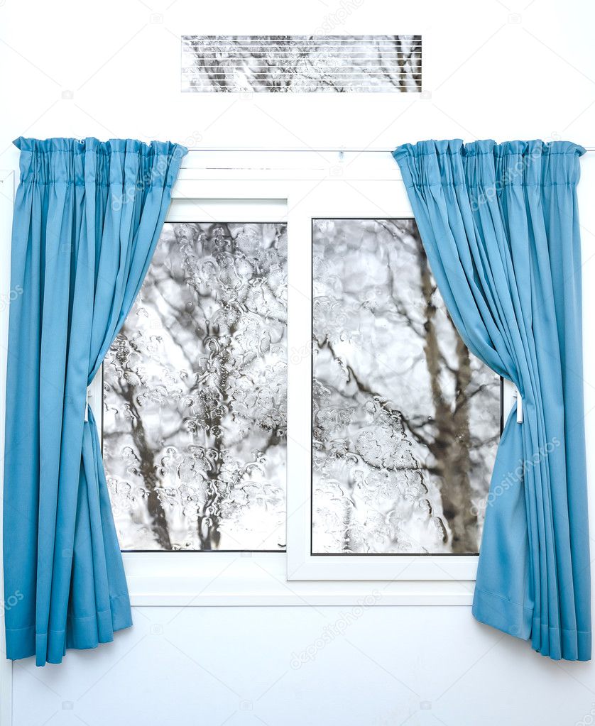 White window with blue curtains on a rainy day