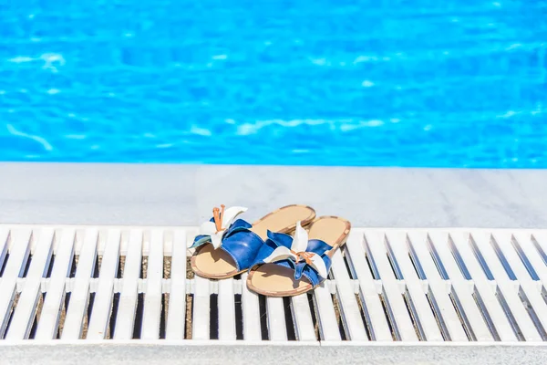 Sandálias femininas com uma flor na borda da piscina — Fotografia de Stock