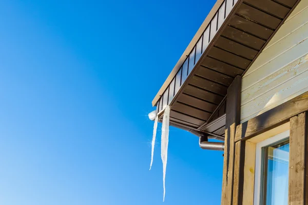 Telhado da casa com pendurado icicles no fundo do céu azul — Fotografia de Stock