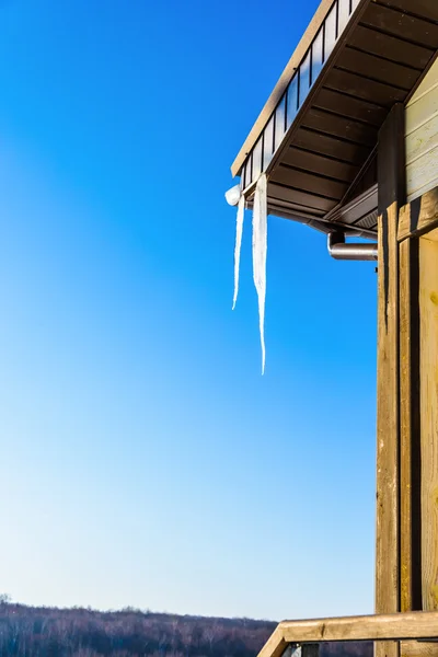 Taket på huset med hängande istappar på blå himmel bakgrund — Stockfoto