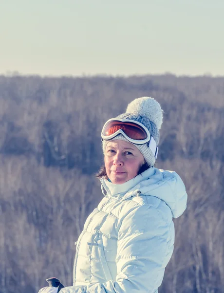 Middle-aged brunette on a hillside in a cap and ski goggles — Stock Photo, Image