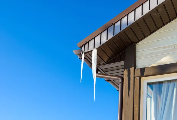 Techo de la casa con carámbanos colgantes sobre fondo azul del cielo — Foto de Stock