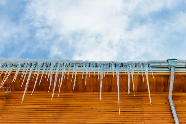 Telhado da casa com pendurado icicles no fundo do céu azul — Fotografia de Stock