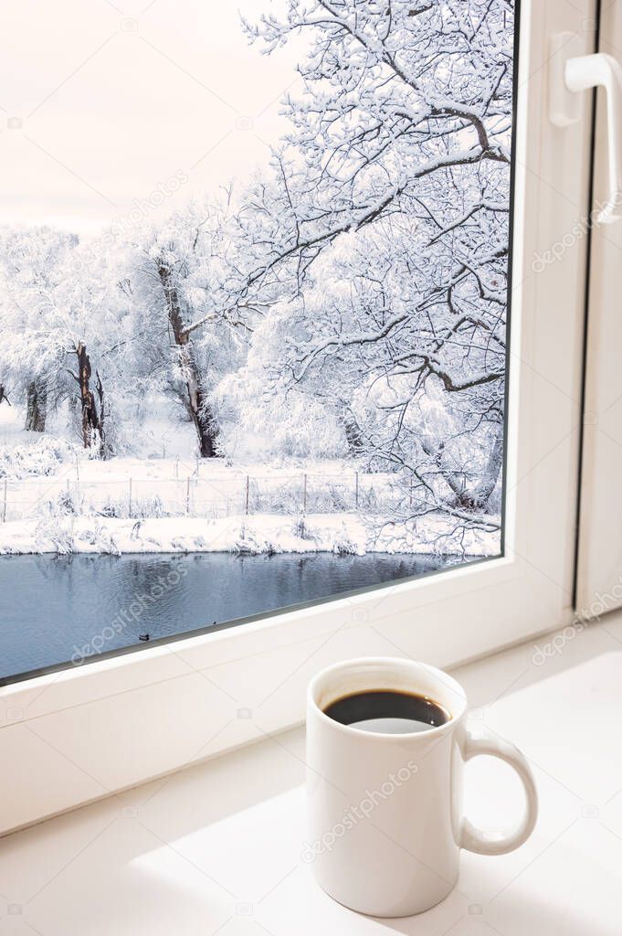 White coffee cup on the windowsill winter landscape outside the window