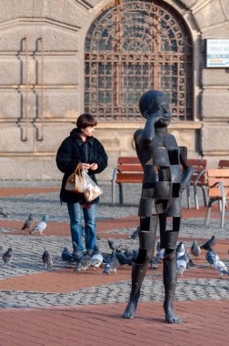 Timisoara, Romanya - 27 Ocak 2016: Telefonda konuşan bir çocuğun heykeli ve sokakta güvercinleri besleyen bir kadın