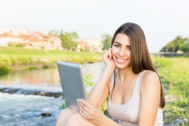 tablet bilgisayar kullanarak nehir kenarında oturan güzel genç kadın