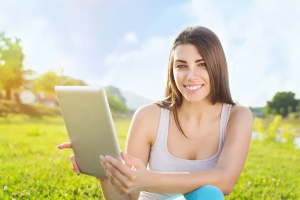 Hermosa mujer joven que se relaja en el parque usando tableta — Foto de Stock