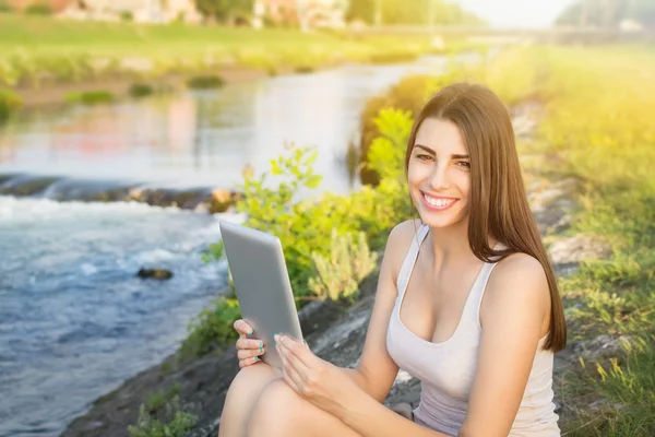 Linda mujer joven usando tableta pc sentado junto al río —  Fotos de Stock