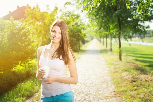 Beautiful young woman holding coffee cup hiking in the park — Stock Photo, Image