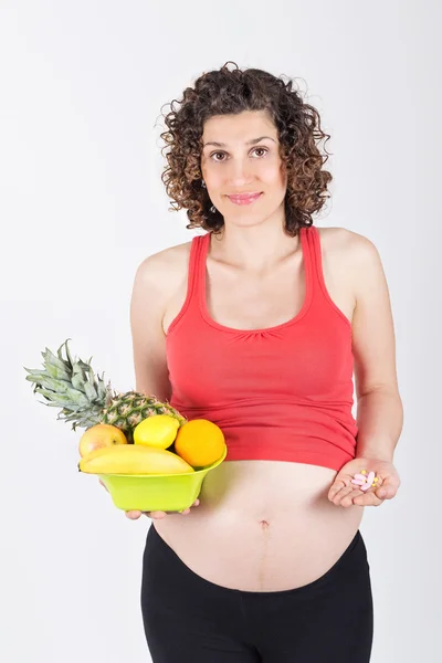 Mulher grávida segurando frutas e pílulas frescas — Fotografia de Stock