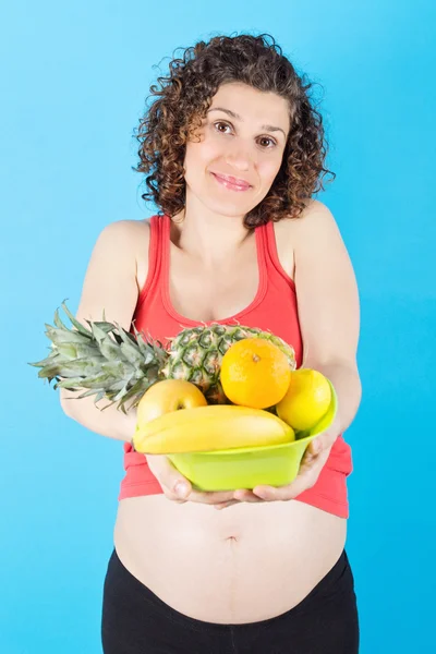 Mujer embarazada feliz con frutas saludables sobre fondo azul — Foto de Stock