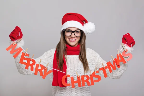 Feliz jovem Santa mulher segurando Feliz Natal texto decoração — Fotografia de Stock