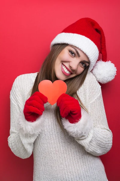 Cute young woman with Santa hat showing red paper heart — Stock Photo, Image