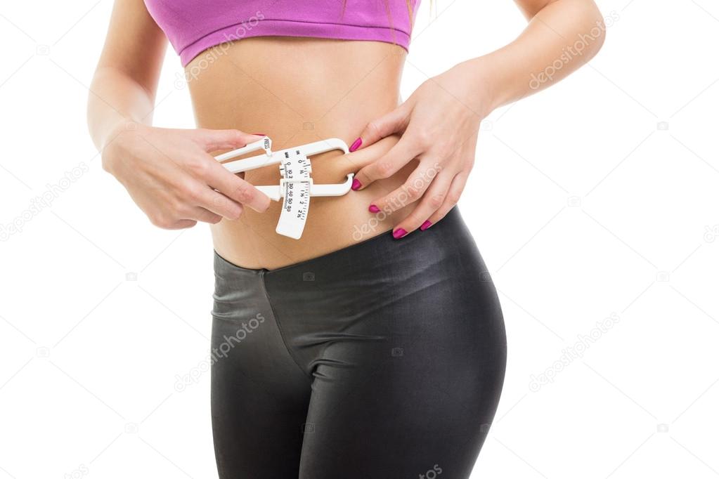 Fit young woman measuring fat on waist using caliper
