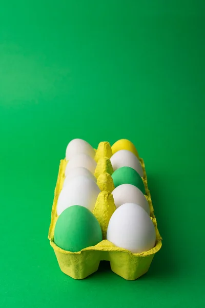 Colorful Easter eggs in yellow carton on green background — Stock Photo, Image