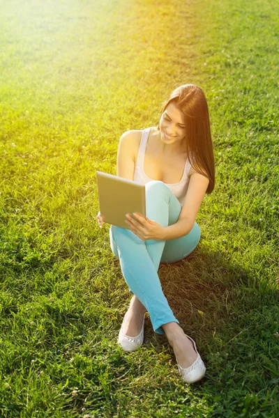 Piękna młoda kobieta z tabletki, siedząc na trawie — Zdjęcie stockowe