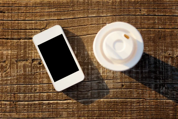 Smartphone und Kaffeetasse auf Holzoberfläche — Stockfoto