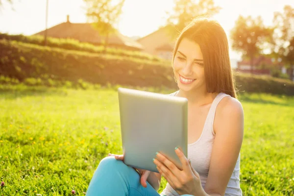 Happy young woman with tablet in park on sunny summer day