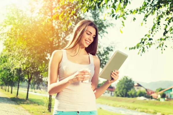 Mujer joven en el parque con tableta y café para llevar — Foto de Stock