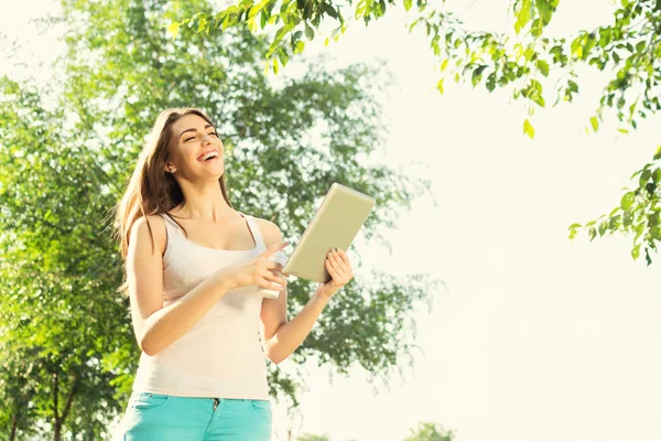 Mujer joven con tableta y café en el parque riendo —  Fotos de Stock