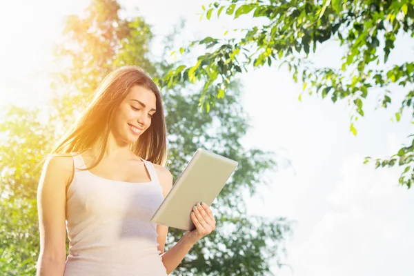 Cute young woman with tablet in park on sunny summer day — Stock Photo, Image