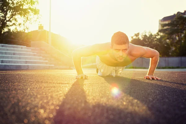 Joven hombre sin camisa en forma haciendo flexiones al aire libre Imagen de archivo