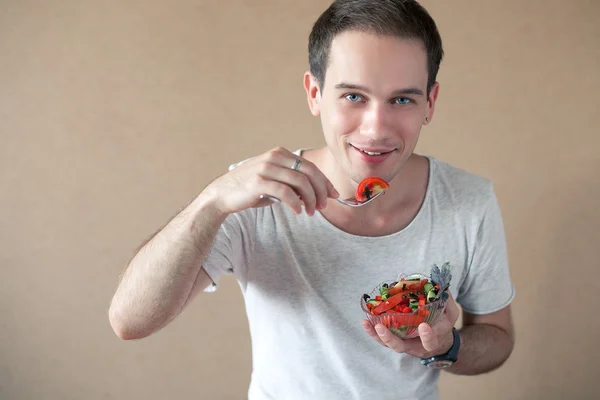 Delgado chico guapo comiendo ensalada sobre fondo de madera. plano de estudio —  Fotos de Stock