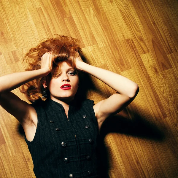 Fashionable young woman lying on wooden floor and looking up. st — Stock Photo, Image