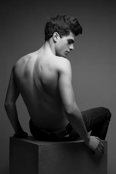 Beautiful (handsome) muscular male model in jeans sitting on a w — Stock Photo, Image