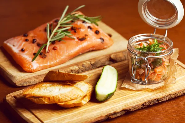 Mason jar with pieces of salmon with fresh cucumber, toasts and