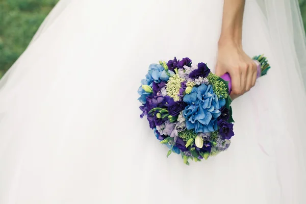 Brudens hand med bröllop bukett med blå blommor över vit klänning — Stockfoto