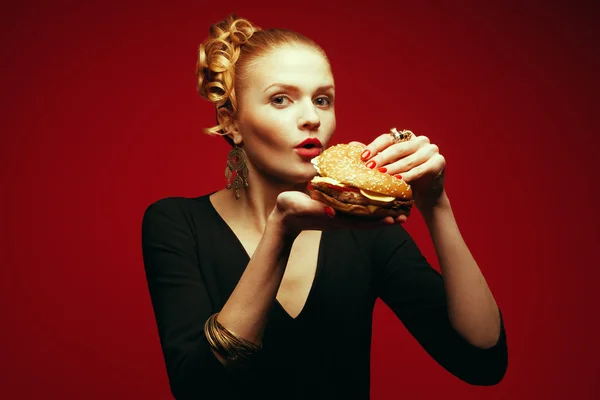 Móda & obžerství koncept. Portrét luxusní zrzavý modelu jíst hamburger — Stock fotografie