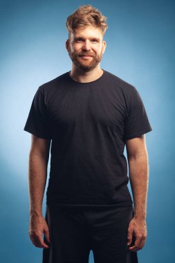 Portrait of charismatic muscular 30-year-old man with red hair posing over blue background. Perfect haircut. Rocker, biker, hipster style. Studio shot