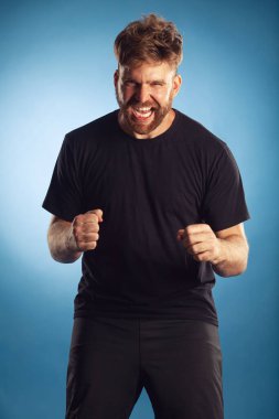 Spor zaferi konsepti. Çığlık atan karizmatik, aktif, 30 yaşında, mavi arka planda elleri havada poz veren birinin duygusal portresi. Mükemmel saç kesimi. Hippi tarzı. Beyaz, parlak bir gülümseme. Stüdyo çekimi