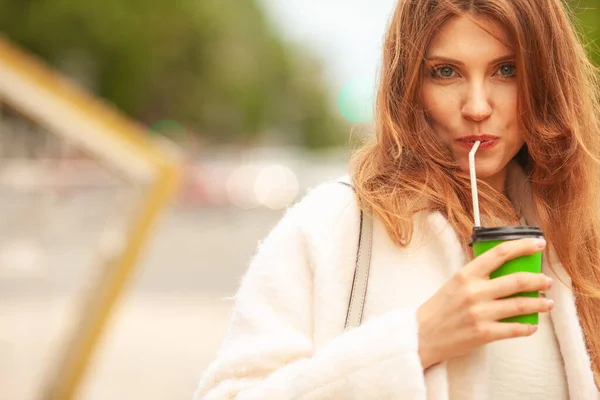 咖啡爱好者的概念 微笑的年轻女子在欧洲城市的街道上喝着热饮 风吹着长发 穿着白色外套的模特 靠近点复制空间 室外开枪 — 图库照片