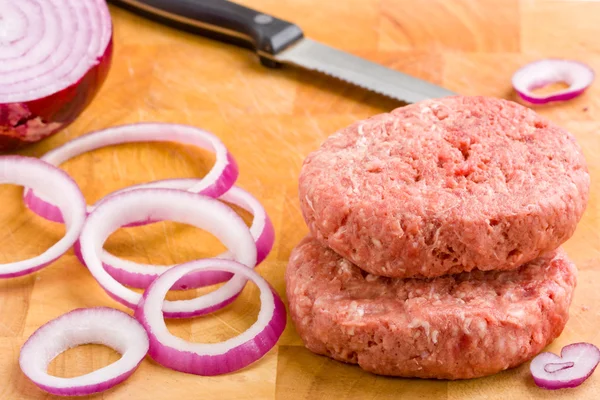 Burger daging sapi mentah dan bawang merah di papan potong . — Stok Foto