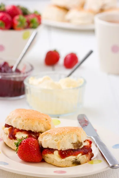 Bollos caseros mermelada de fresa, fresas de crema coagulada y té . Imagen De Stock