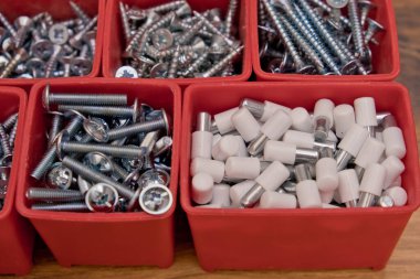 Tahta bir arka planda kırmızı plastik tepsi kutusunda çeşitli boyutlarda vida, cıvata, tahta çiviler ve tahta çiviler var. Mobilyalar için montaj seti. Seçici odak.
