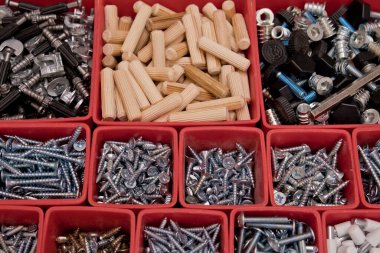 Tahta bir arka planda kırmızı plastik tepsi kutusunda çeşitli boyutlarda vida, cıvata, tahta çiviler ve tahta çiviler var. Mobilyalar için montaj seti. Seçici odak.