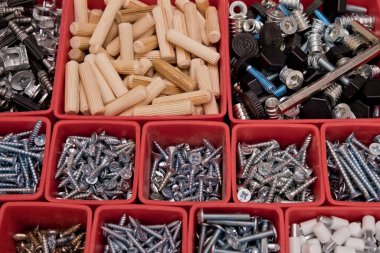 Tahta bir arka planda kırmızı plastik tepsi kutusunda çeşitli boyutlarda vida, cıvata, tahta çiviler ve tahta çiviler var. Mobilyalar için montaj seti. Seçici odak.