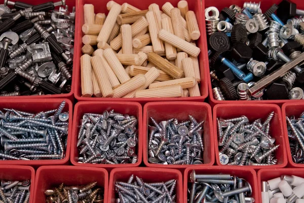 Tahta bir arka planda kırmızı plastik tepsi kutusunda çeşitli boyutlarda vida, cıvata, tahta çiviler ve tahta çiviler var. Mobilyalar için montaj seti. Seçici odak.